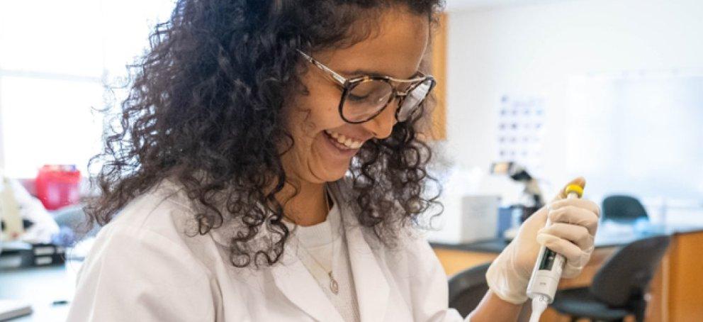 In a lab with others, a faculty member in the middle of an experiment, stands with a big smile on her face.